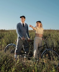 a man and woman standing next to a bicycle in a field